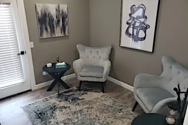Interior therapy space with gray walls, two upholstered armchairs, side table, framed art, and closet door.