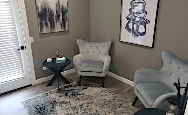 Interior therapy space with gray walls, two upholstered armchairs, side table, framed art, and closet door.