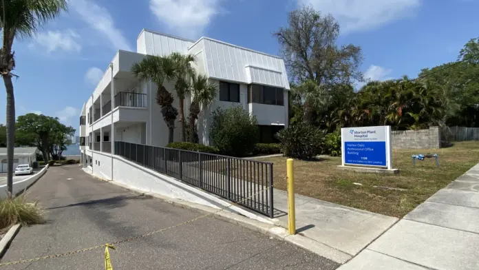 Exterior view of modern multi-story white office building with landscaping, parking area, and facility signage