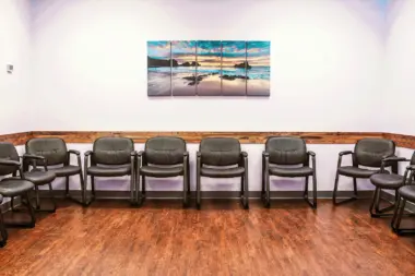 Interior seating room with rows of gray chairs, wood paneling, scenic beach artwork, and purple ambient lighting