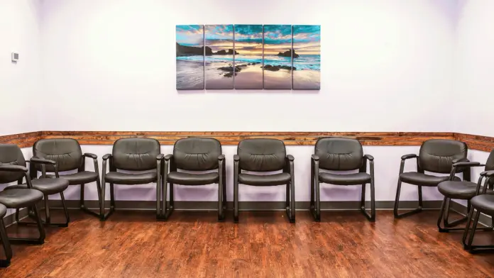 Interior seating room with rows of gray chairs, wood paneling, scenic beach artwork, and purple ambient lighting