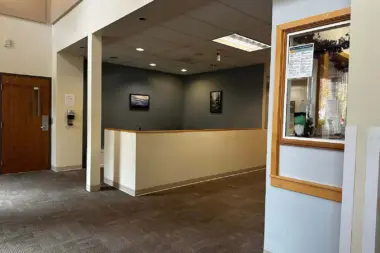 Interior reception desk with counter, neutral walls, wooden door, and hallway access