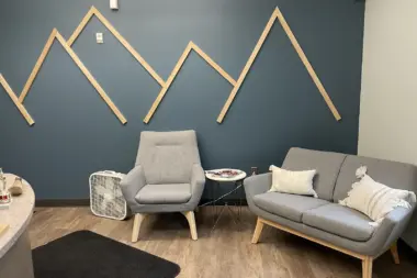 Interior lounge with upholstered furniture, wooden mountain wall art installation, and side table in modern aesthetic space.