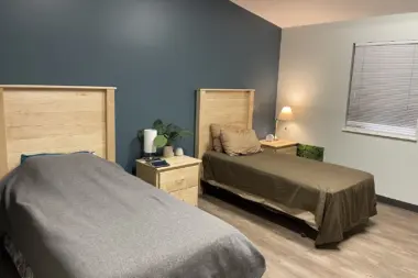 Interior bedroom with twin beds, wood headboards, nightstands with lamps, plant décor, and neutral color palette.