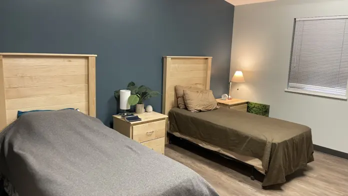 Interior bedroom with twin beds, wood headboards, nightstands with lamps, plant décor, and neutral color palette.