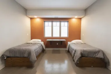 Interior bedroom with twin beds, orange accent wall, window, and natural lighting