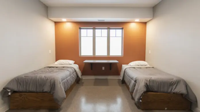 Interior bedroom with twin beds, orange accent wall, window, and natural lighting