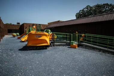 Outdoor play area featuring orange AeroGLIDER equipment structure and green safety fencing