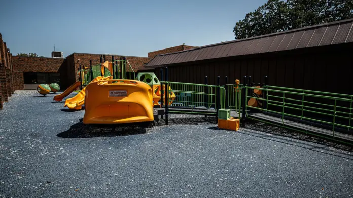 Outdoor play area featuring orange AeroGLIDER equipment structure and green safety fencing