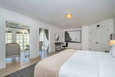 Interior bedroom with king bed, workspace with desk, seating area, and French doors to outdoor patio