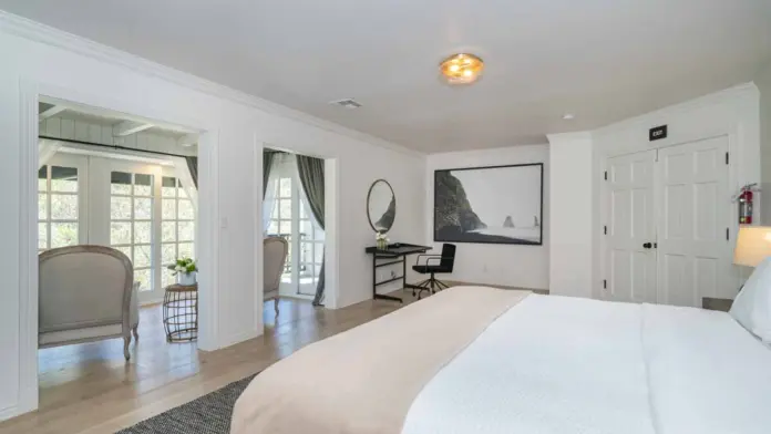 Interior bedroom with king bed, workspace with desk, seating area, and French doors to outdoor patio