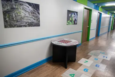 Interior hallway with nature artwork, game table, numbered floor markers, colored doors, and blue trim design