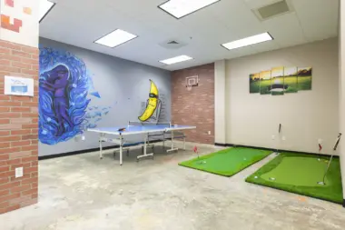 Interior activity room with abstract mural art, ping-pong table, and indoor putting green