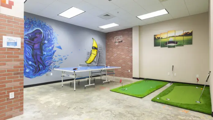 Interior activity room with abstract mural art, ping-pong table, and indoor putting green