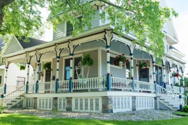 Exterior white Victorian-style house with blue-trimmed porch, white railings, and hanging flower baskets
