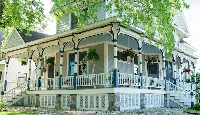 Exterior white Victorian-style house with blue-trimmed porch, white railings, and hanging flower baskets