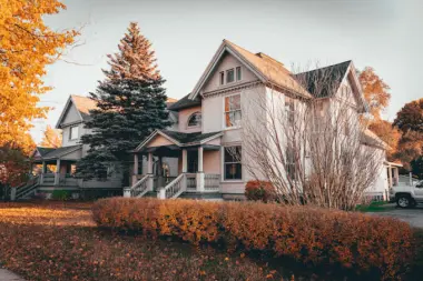 Exterior of Victorian-style two-story house with white siding, gabled roof, and autumn foliage surrounding grounds