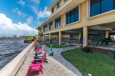 Exterior patio seating with pink Adirondack chairs, landscaping, grass, pathways, and river view near yellow building.
